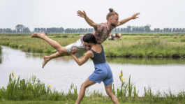 Dans, if you scream i whisper: een danseres lift een danser met op de achtergrond de polder