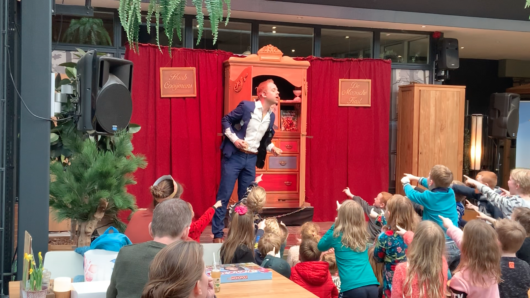Goochelaar Huub Cooijmans, met magische kast op podium met kinderen